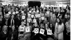 Black and white image of a group of women smiling and posing with poster letters that spell out "#MindOfMyOwn".
