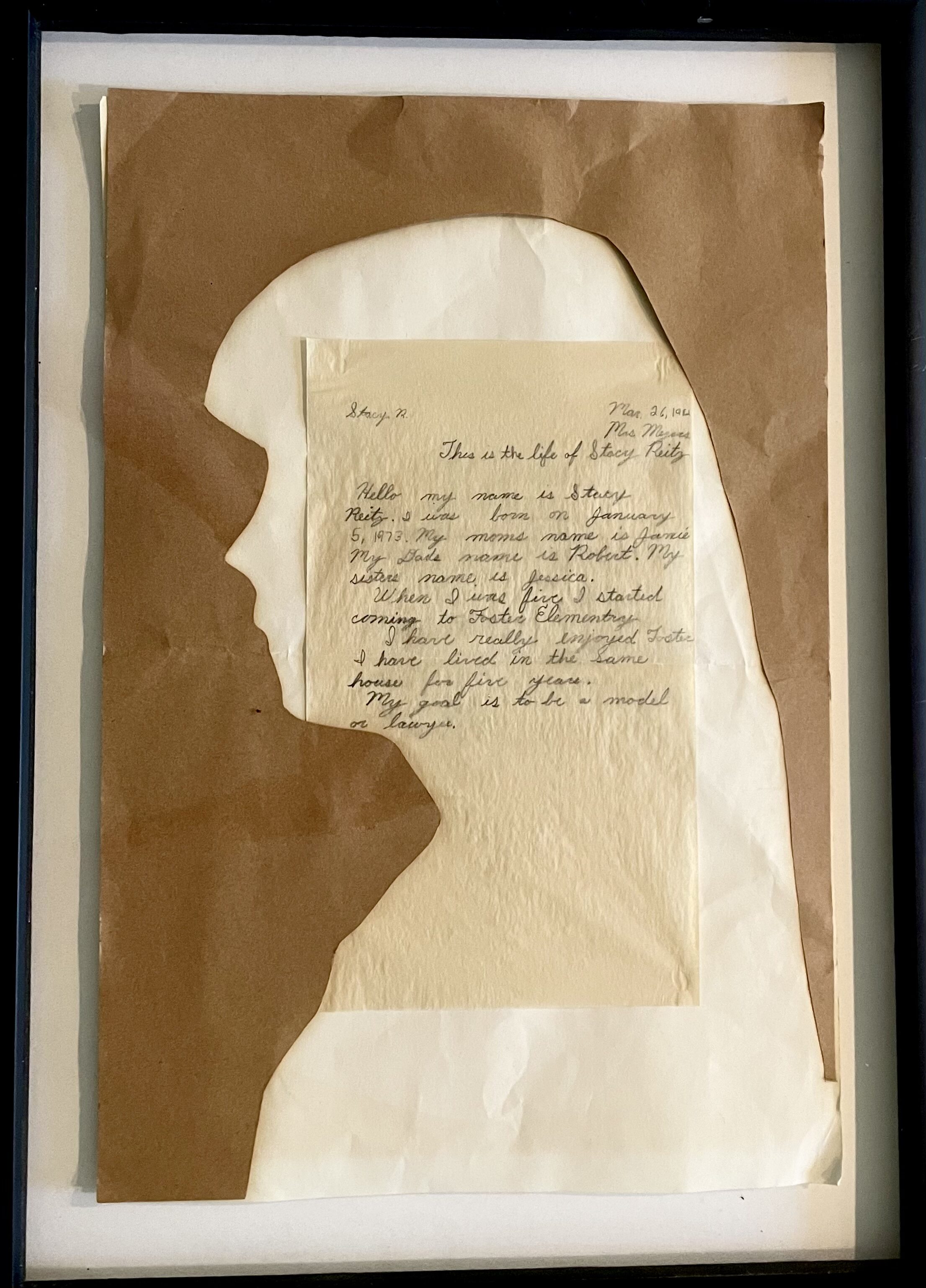 Color photo, paper cutout of a woman's side profile with a handwritten letter on top.