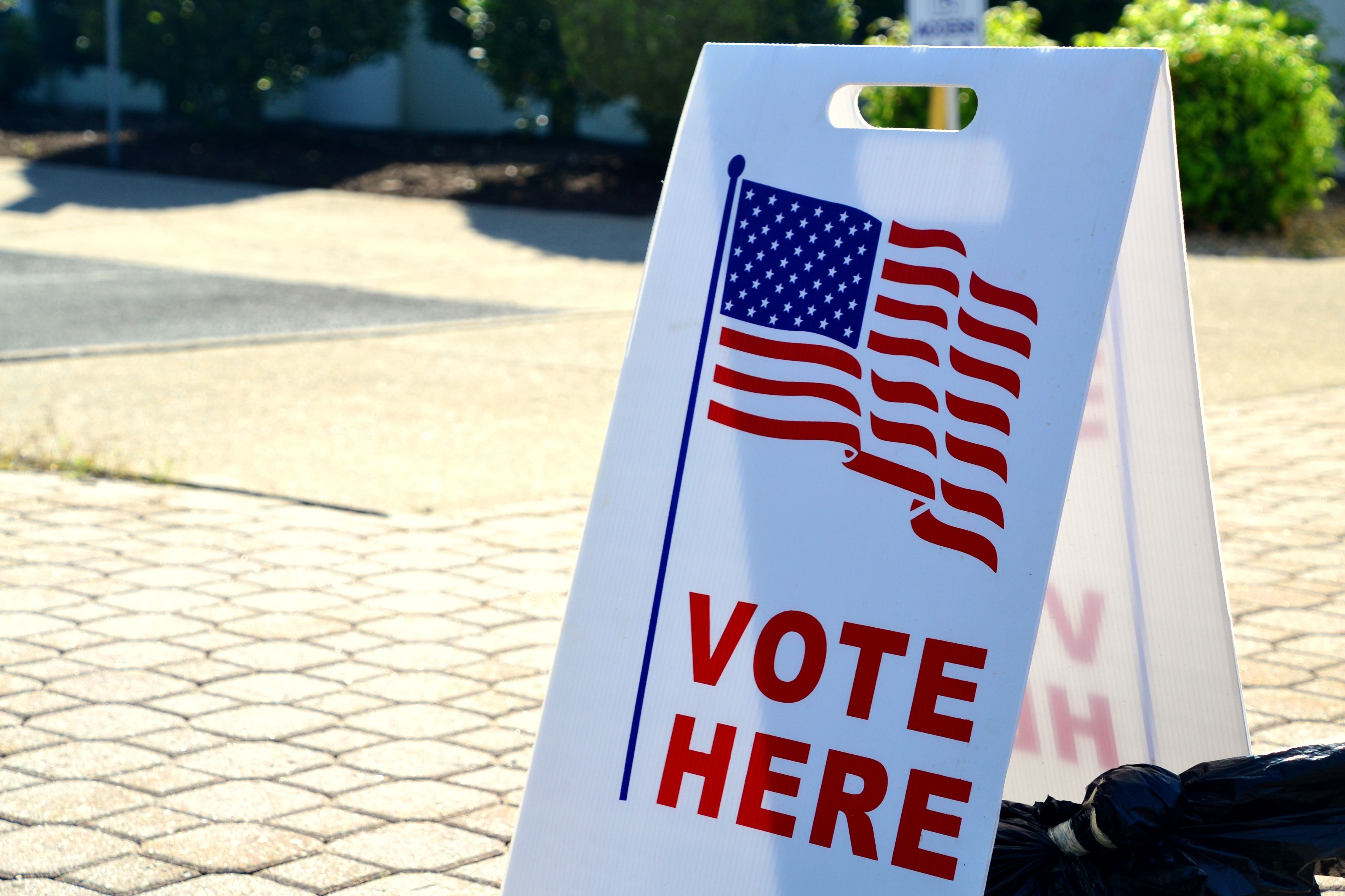 A sign that says "Vote Here" on a walking path.
